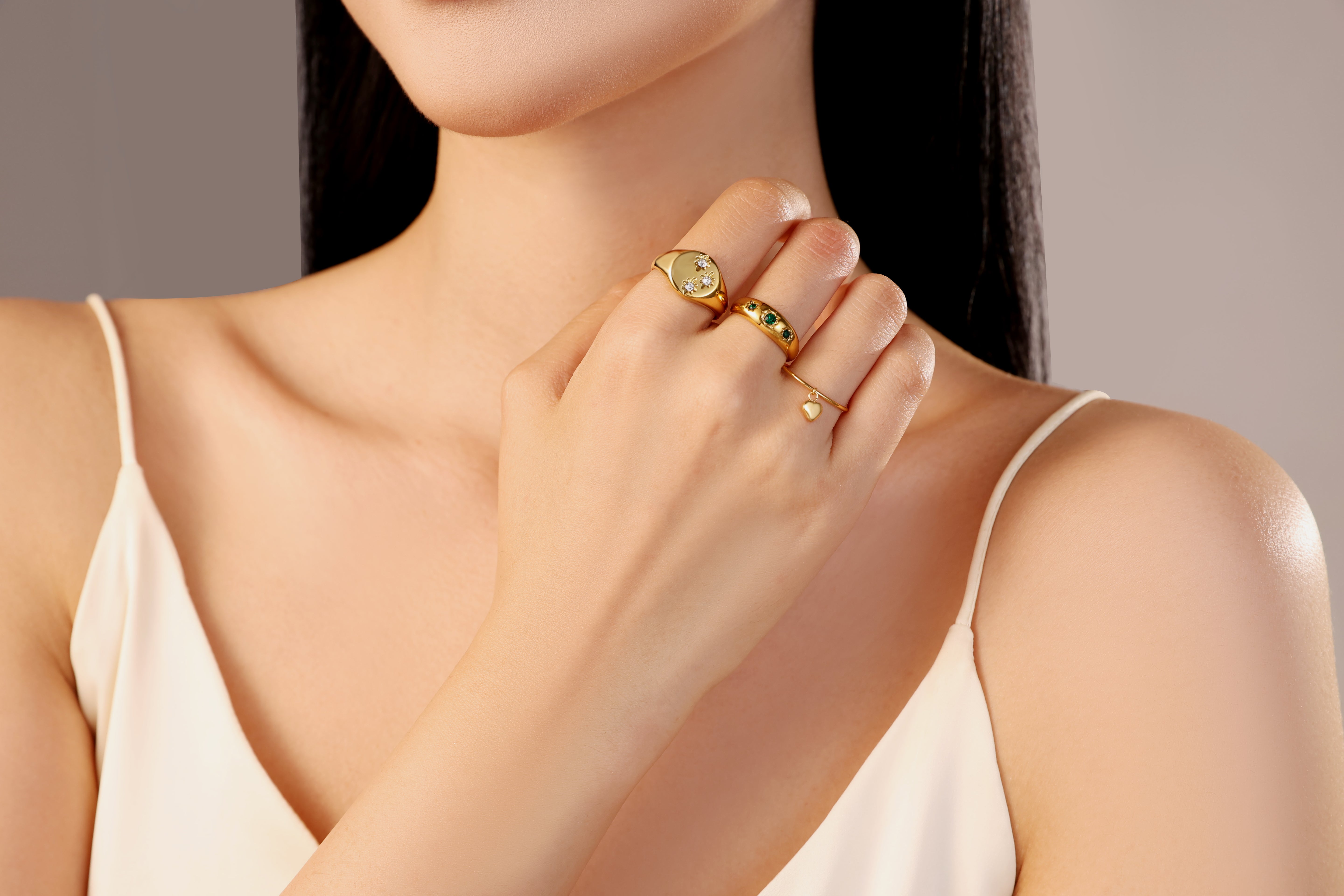 model wearing three gold waterproof stainless steel rings with heart charm green stones signet