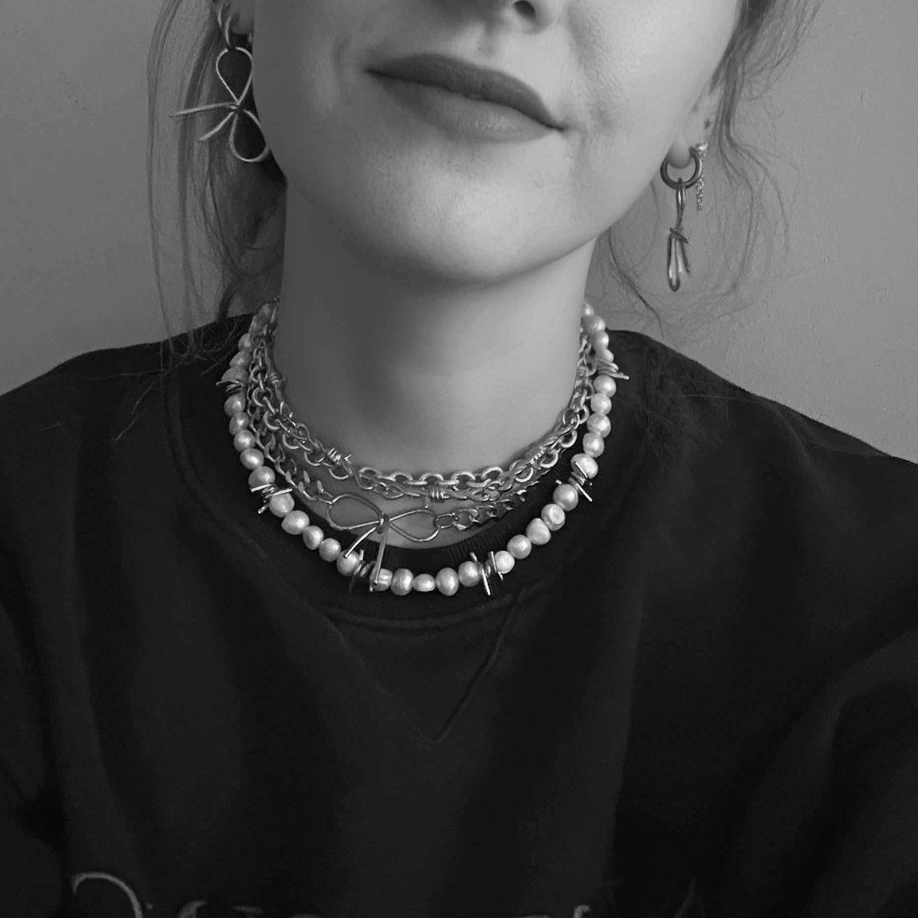 Black and white portrait of a person wearing multiple necklaces and earrings.