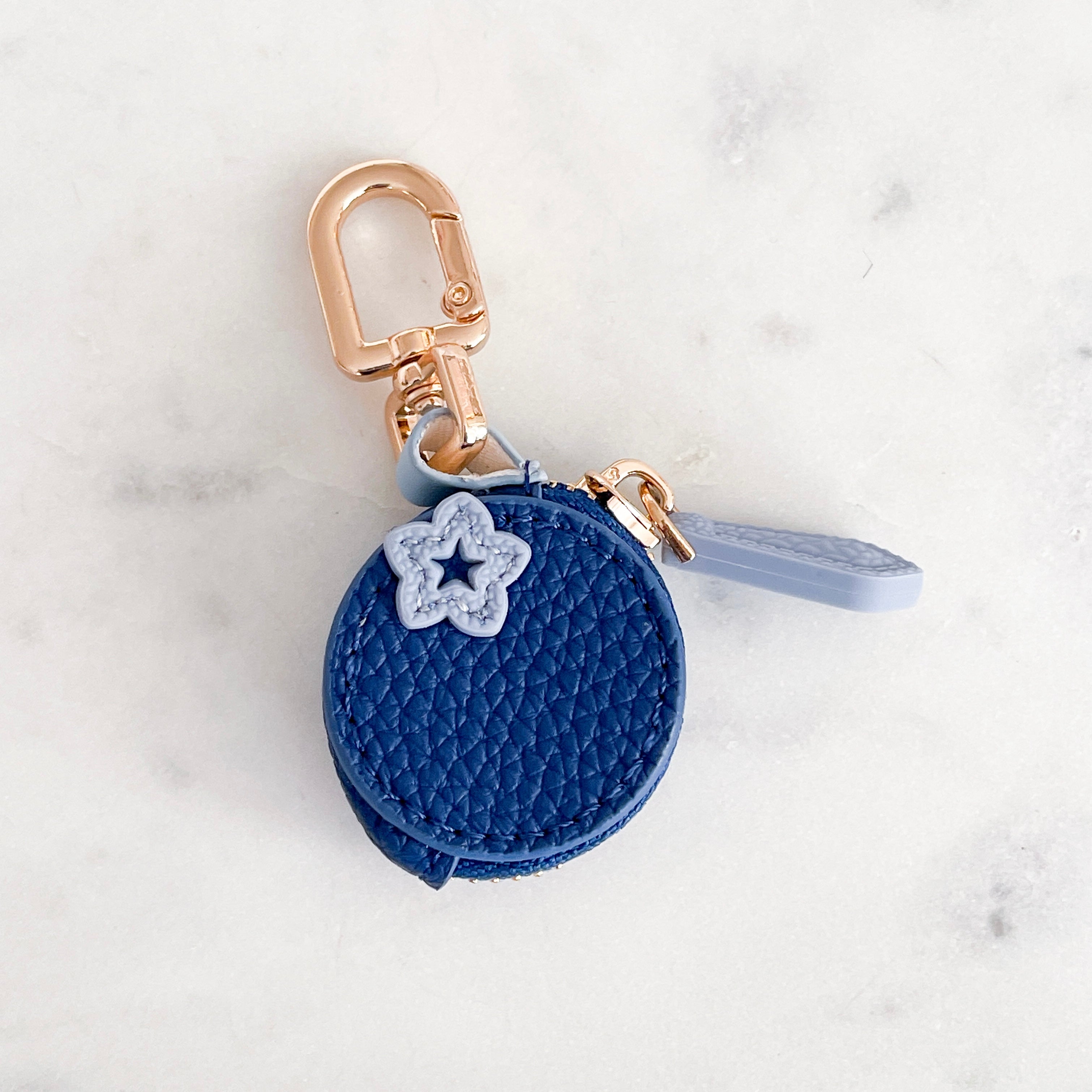 Blue keychain shaped like a blueberry with gold zip and keyring charm on a light gray background