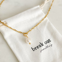 Gold necklace with a freshwater pearl pendant on a 'break out jewellery' branded dustbag 