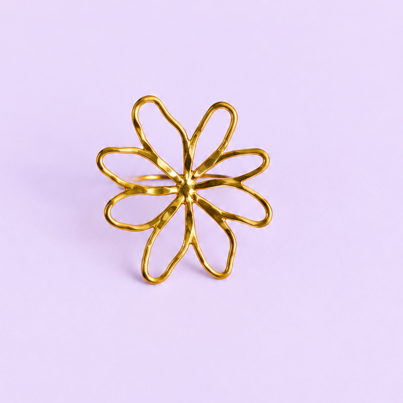 A gold metal flower-shaped ring with six open petals, centered on a solid light purple background.