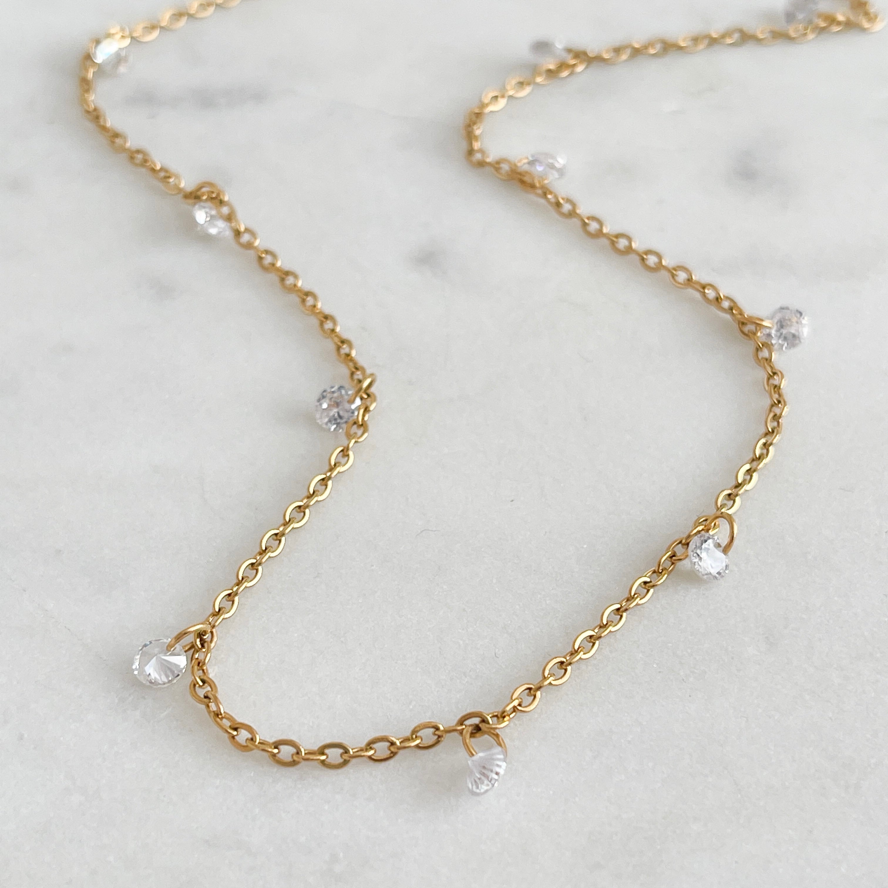 Gold chain necklace with small crystals on a marble surface