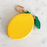 Yellow lemon-shaped keychain with a green leaf on a marble surface