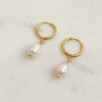 Gold hoop earrings with pearl charms on a light background