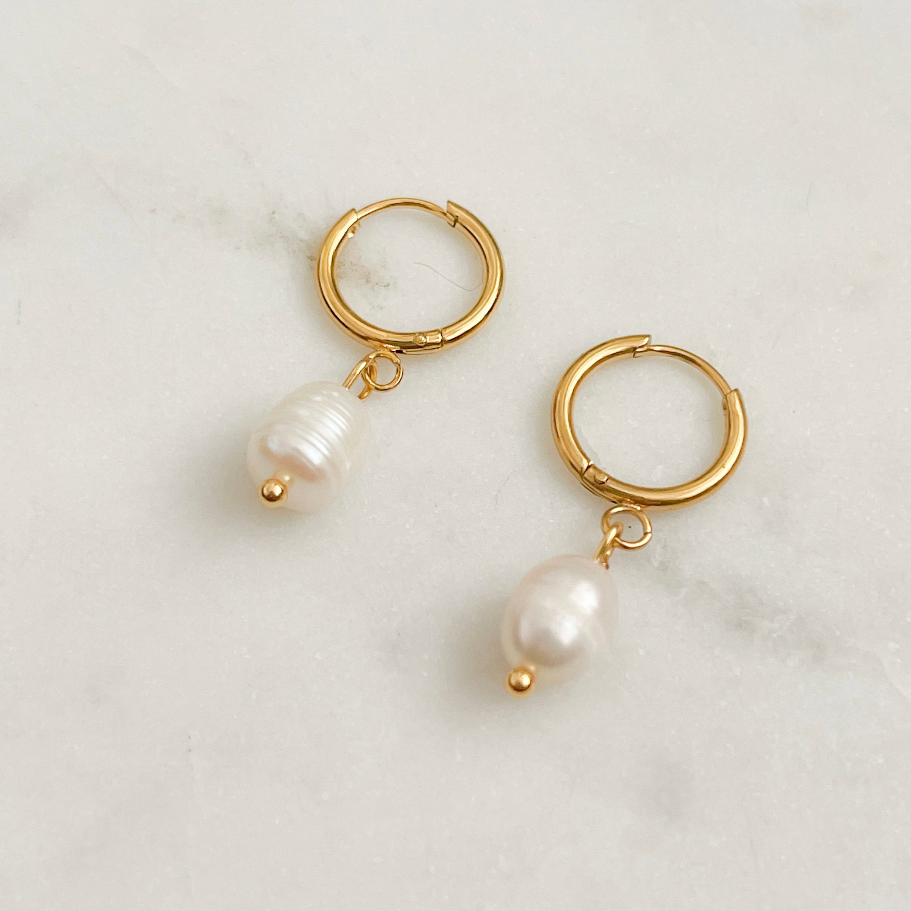Gold hoop earrings with pearl charms on a light background
