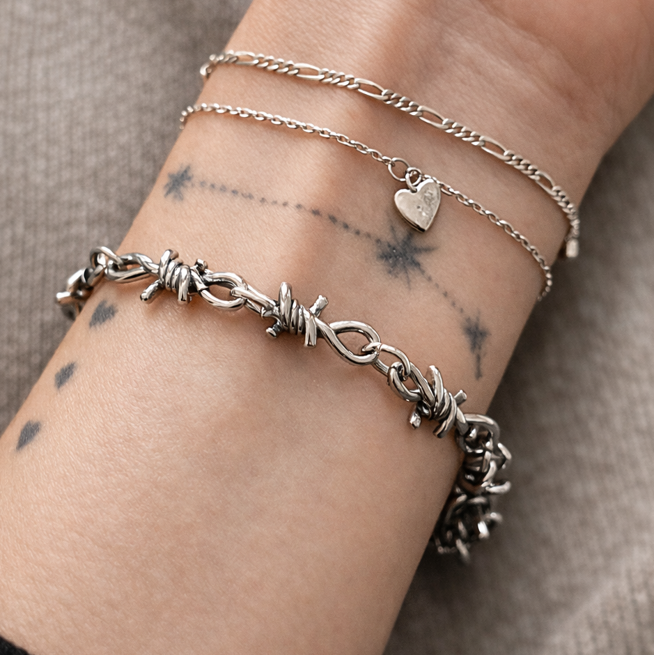 Close-up of a wrist wearing multiple silver bracelets on a neutral background