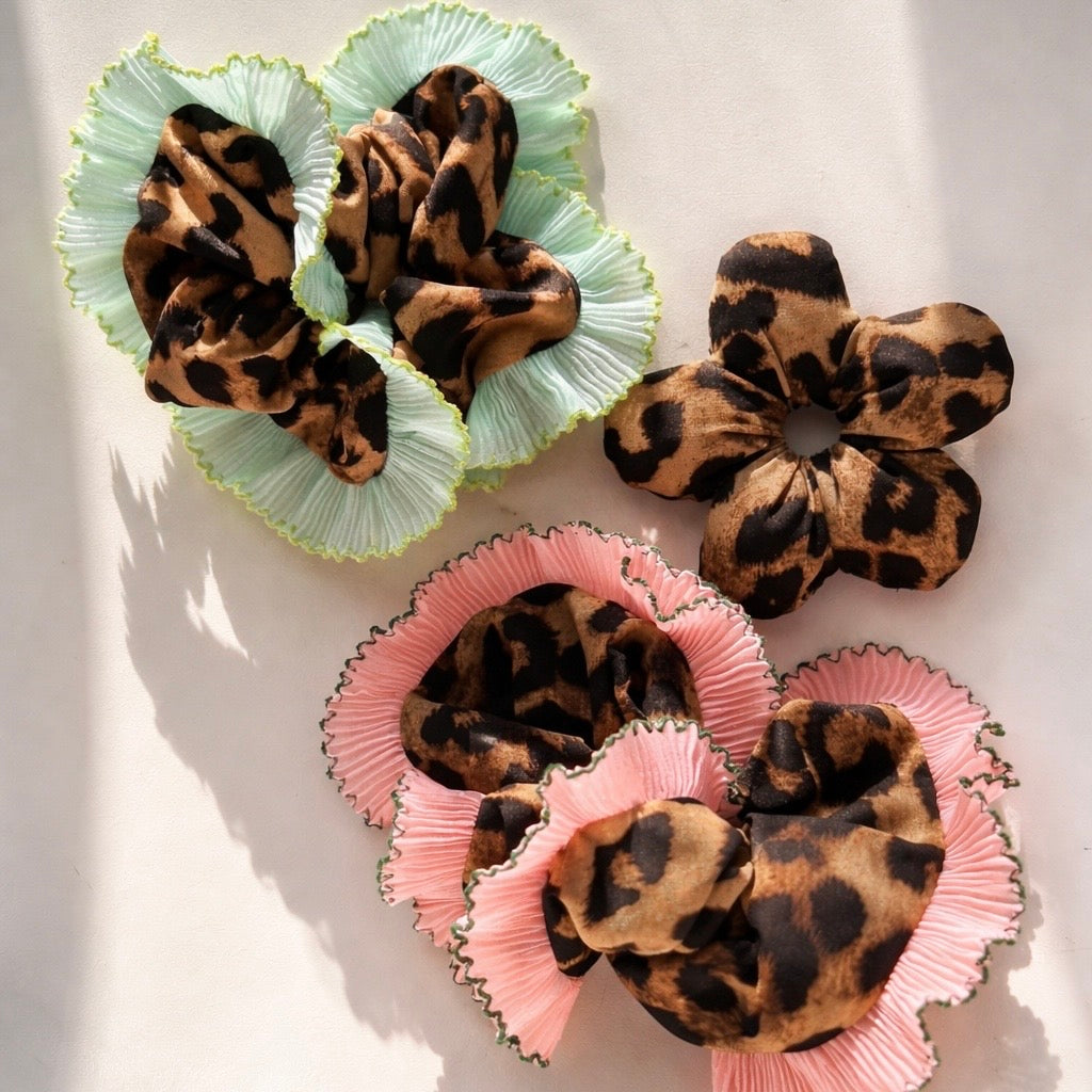 three leopard scrunchies, two have colourful trim (green and pink) one is shaped like a flower