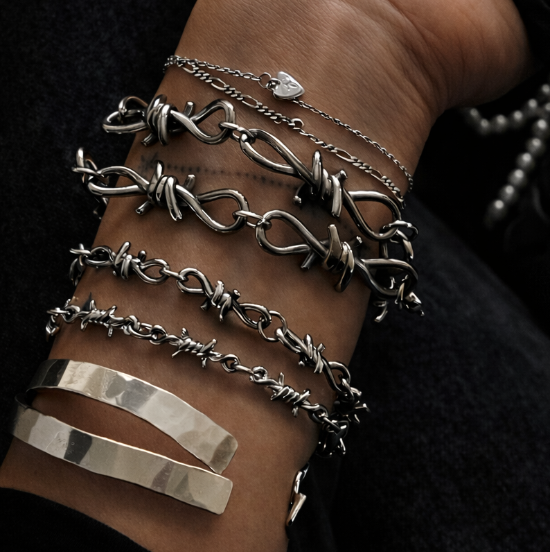 Hand wearing multiple silver bracelets on a dark background